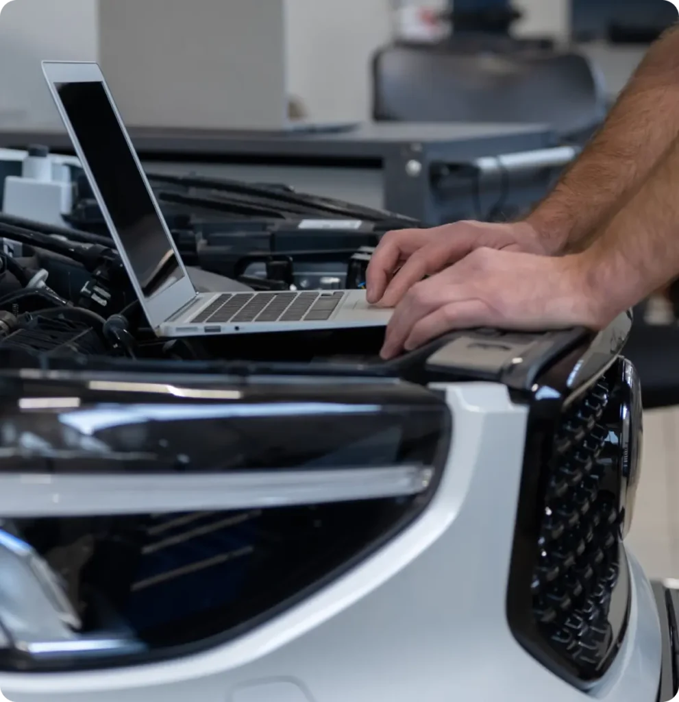 Car diagnostics and electrical repair, auto repair in Springfield, OR, at Absolute Air & Auto Repair. A person uses a laptop placed on the hood of a car with the hood open, likely performing diagnostics or repairs in a garage or workshop setting.