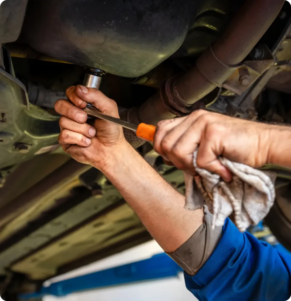 Preventative maintenance, auto repair in Springfield, OR, at Absolute Air & Auto Repair. Mechanic’s hands using a wrench to work underneath a car, holding a cloth in one hand and wearing a blue sleeve, with the car raised on a lift.
