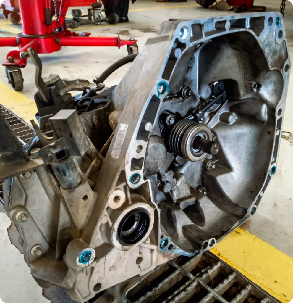 Transmission repair and replacement, auto repair in Springfield, OR, at Absolute Air & Auto Repair. A close-up view of a car transmission assembly placed on a workshop floor, showing mechanical parts and bolts, with workshop equipment visible in the background.