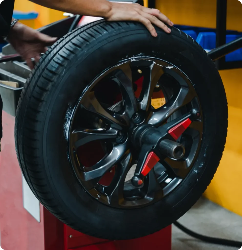 Tire sales & services, auto repair in Springfield, OR, at Absolute Air & Auto Repair. A person holds a car tire mounted on a wheel balancing machine in an auto repair shop, with tools and equipment visible in the background.