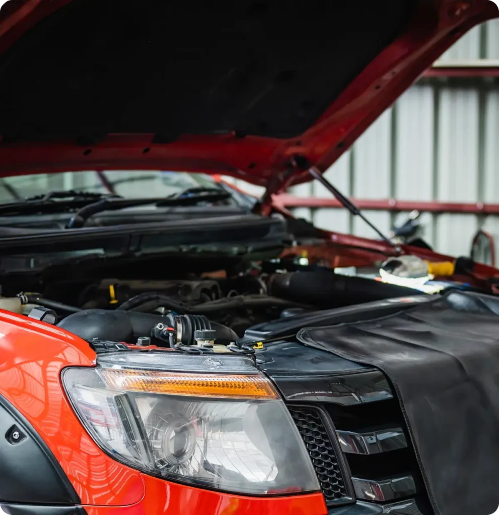 Diesel repair, auto repair in Springfield, OR, at Absolute Air & Auto Repair. A close-up of a red car with its hood open, showing the engine and engine bay inside a garage or workshop. A black protective cover is draped over the front fender.