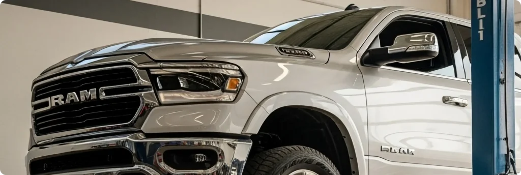 Domestic auto repair in Springfield, OR, at Absolute Air and Auto Repair. A white RAM pickup truck is raised on a lift inside a garage or service center, showing its front and side with chrome accents and large mirrors.