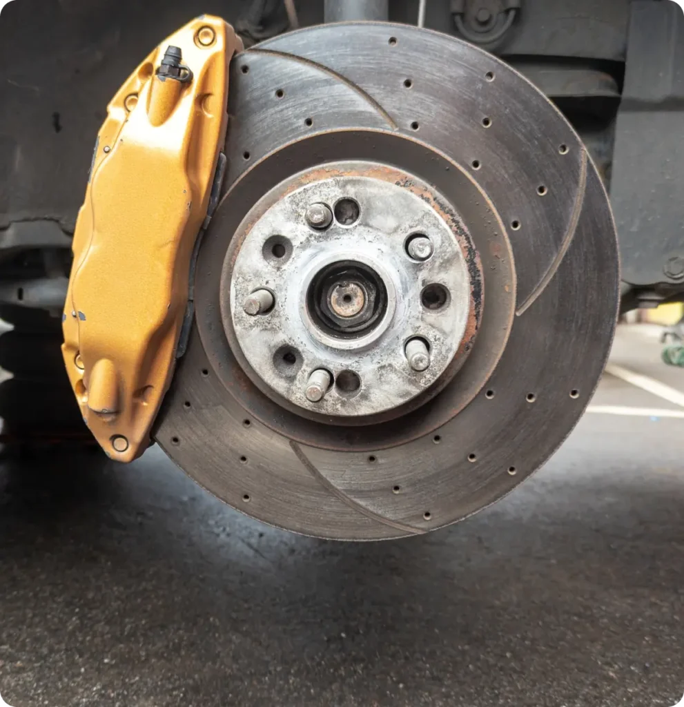 Brake repair, auto repair in Springfield, OR, at Absolute Air & Auto Repair. A close-up of a cars exposed brake disc and gold-colored brake caliper, with the wheel removed, showing detailed grooves and bolts, on a dark pavement background.