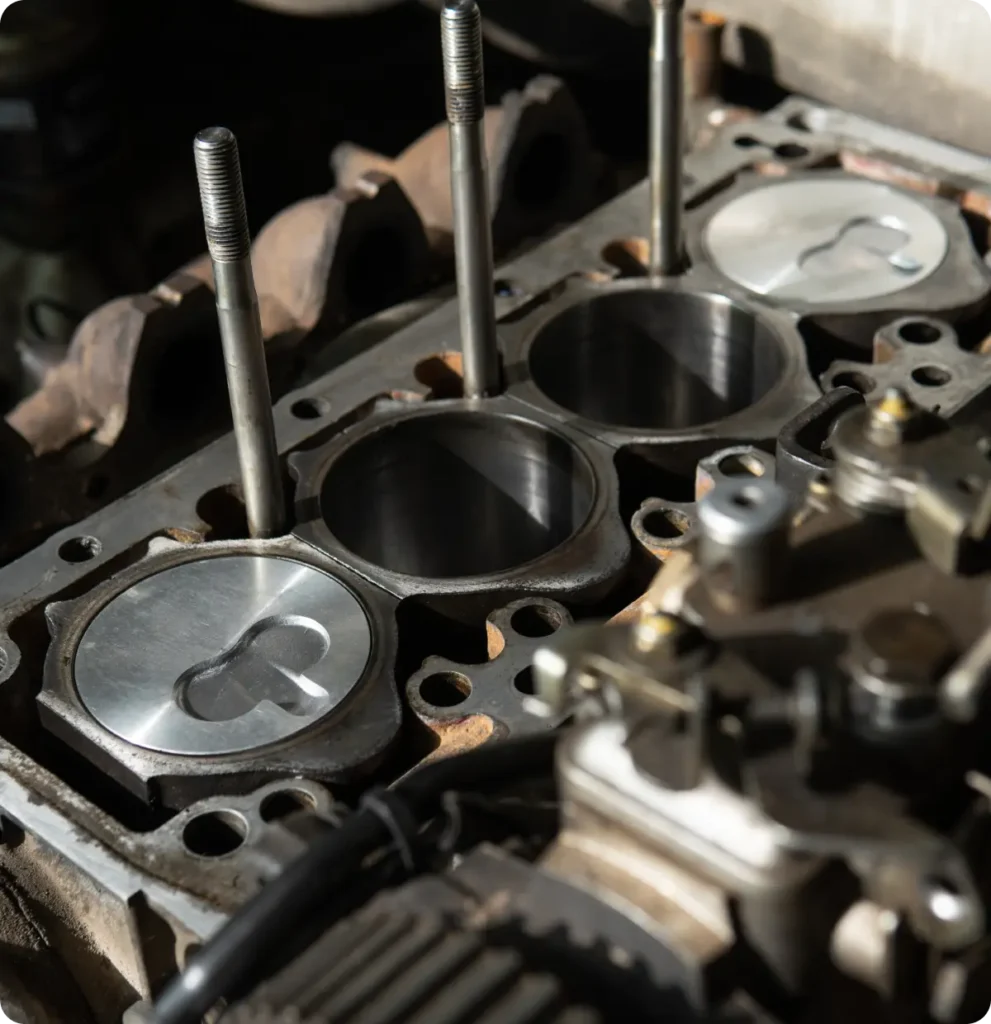 Engine repair and replacement, auto repair in Springfield, OR, at Absolute Air & Auto Repair. Close-up of an engine block showing four cylinders, two with metal pistons exposed and two with pistons retracted, surrounded by metal rods and various engine components.