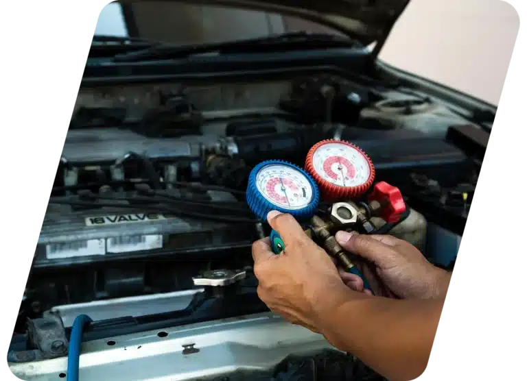 A person uses a pressure gauge manifold to check or service the air conditioning system under the hood of a car.
