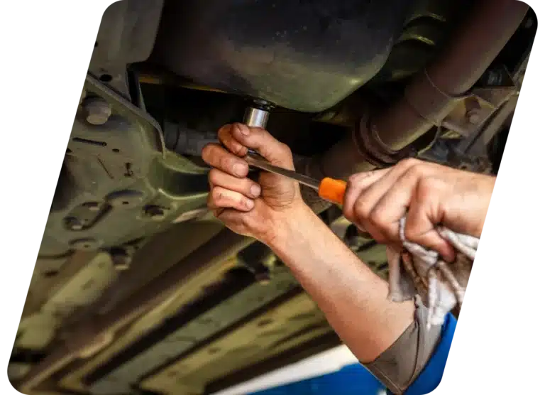 A person’s hands using tools to work on the underside of a vehicle, possibly performing maintenance or repairs.