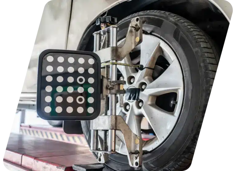 A car wheel with an alignment tool attached, positioned on a workshop lift for a wheel alignment check.